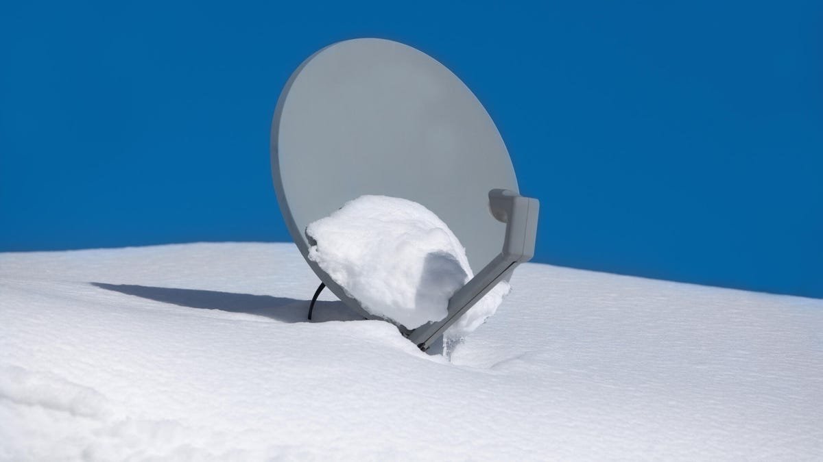 Snow-covered satellite dish on a snowy roof, lit by early morning sunshine.